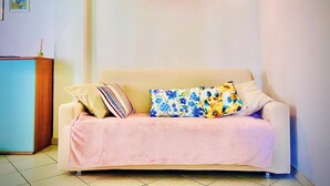 A living room with a beige sofa, a pink blanket, and a floral pillow. There is a wall-mounted light fixture and a small framed picture on the wall. - Comfortable two-room apartment near Santa Maria Novella station (Firenze)