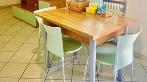 A dining area with a wooden table, four white chairs, a wooden cabinet with a mirror, and a window with curtains. - Comfortable two-room apartment near Santa Maria Novella station (Firenze)