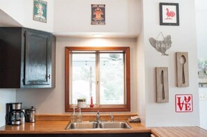 Una cocina con ventana, armarios de madera, un fregadero y diversos utensilios.