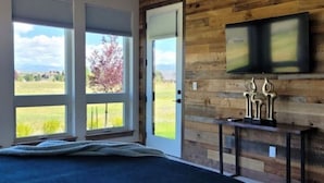 Quarto com uma cama grande, uma parede de madeira, uma TV montada sobre um console e janelas amplas com vista para o exterior.