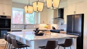 Uma cozinha moderna com uma ilha grande, eletrodomésticos pretos e iluminação pendente.