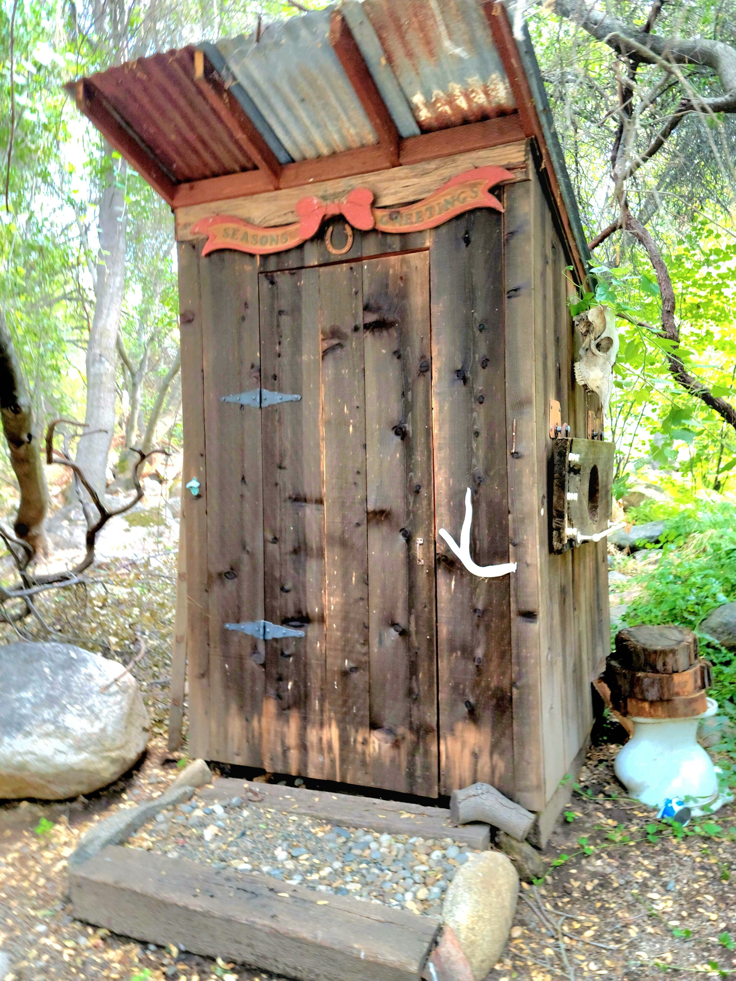 Eine rustikale Holzhütte mit Wellblechdach, einer Holztür mit Metallriegel und einem kleinen Podest davor.