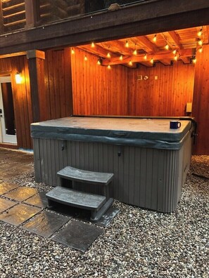 Un bain à remous avec des marches, entouré d’une terrasse en bois et illuminé de guirlandes lumineuses.