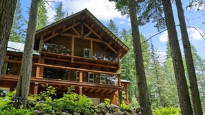 A log cabin with a balcony, surrounded by trees and rocks. - Perry River Lodge, Your Riverside Retreat (Columbia-Shuswap)