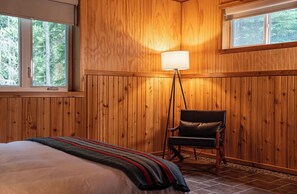 Une pièce aux murs lambrés, contenant un lit, une chaise et un lampadaire.