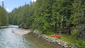 A river with clear water, surrounded by dense green forest and a stone wall. - Perry River Lodge, Your Riverside Retreat (Columbia-Shuswap)