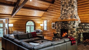 A log cabin interior with a stone fireplace, leather sectional sofa, and wooden walls. - Perry River Lodge, Your Riverside Retreat (Columbia-Shuswap)