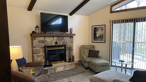 A living room with a stone fireplace, a television, and a large window with blinds. - Cozy Lakefront Home; Close to skiing and waterparks (Blakeslee)