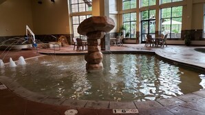 Une piscine intérieure ornée d’une sculpture rocheuse originale en son centre, entourée d’espaces de détente et de grandes fenêtres.