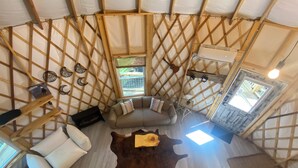 A yurt-style room with a sofa, a wooden table, and a cowhide rug. - Windsong yurt, in the treetops, hottub on the top deck, petfriendly, stargazing (Hillsville)