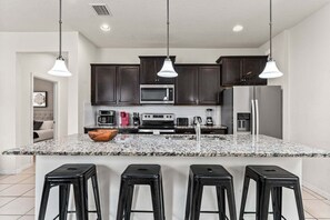 A modern kitchen with dark cabinets, a granite countertop, a central island with stools, and overhead pendant lighting.