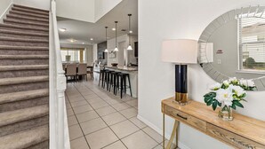 A modern interior with a staircase, a dining area, a kitchen, and a console table with a lamp and flowers. - Family Paradise Close to Disney w Resort Amenities (Kissimmee)