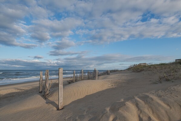 A sandy beach with a wooden fence and a wooden structure in the background.