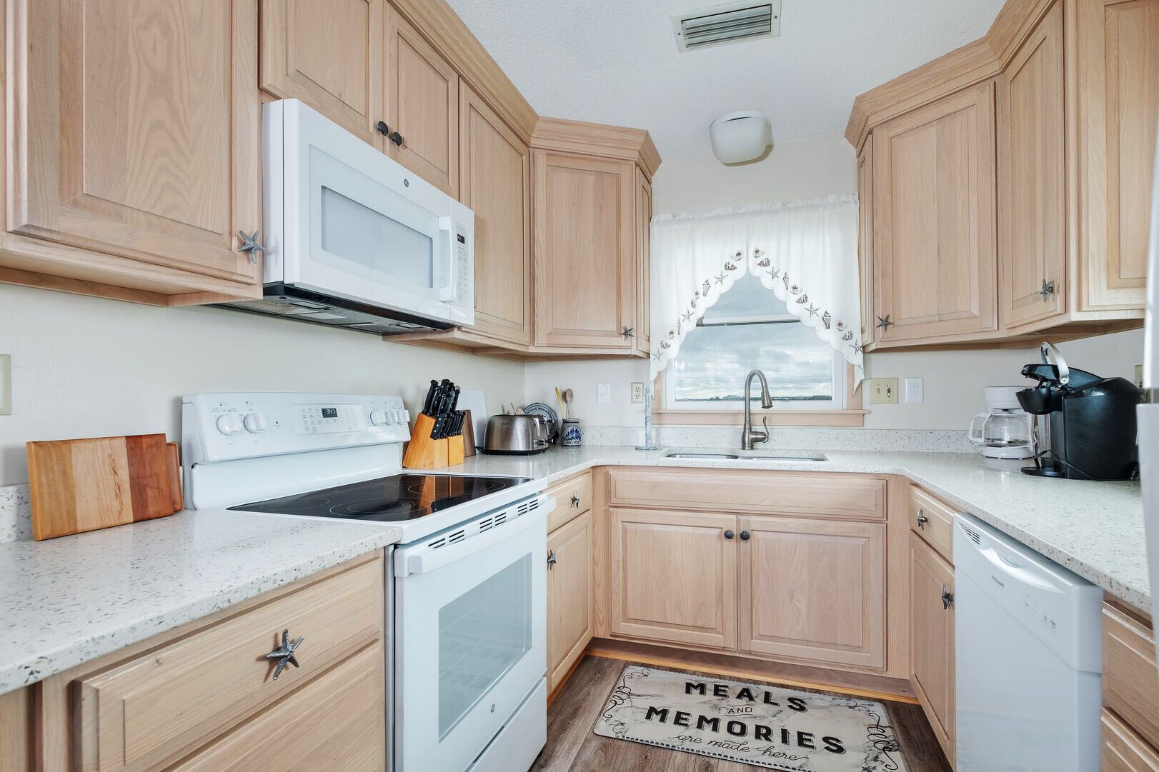 A kitchen with wooden cabinets, a microwave, stove, sink, and a window with a decorative curtain.