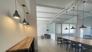 Un espacio de oficina moderno con una larga mesa de madera y sillas negras, iluminación suspendida y un techo alto con vigas a la vista.