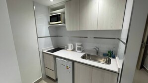 Una kitchenette compacta con microondas, cafetera, lavamanos y un refrigerador pequeño.
