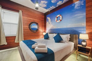 A bedroom with a wooden wall, a bed with blue and white bedding, a nightstand with a lamp, and a life preserver on the wall. - Discounted 12BR w Barbie Castle/Dino Slide/Games (Kissimmee)