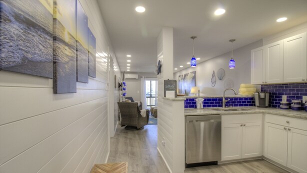 Cozinha moderna com armários brancos, lava-louças de aço inoxidável e painel de azulejos azuis.