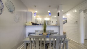 Uma sala de jantar com mesa e cadeiras, uma cozinha ao fundo e um corredor que leva a outro quarto.
