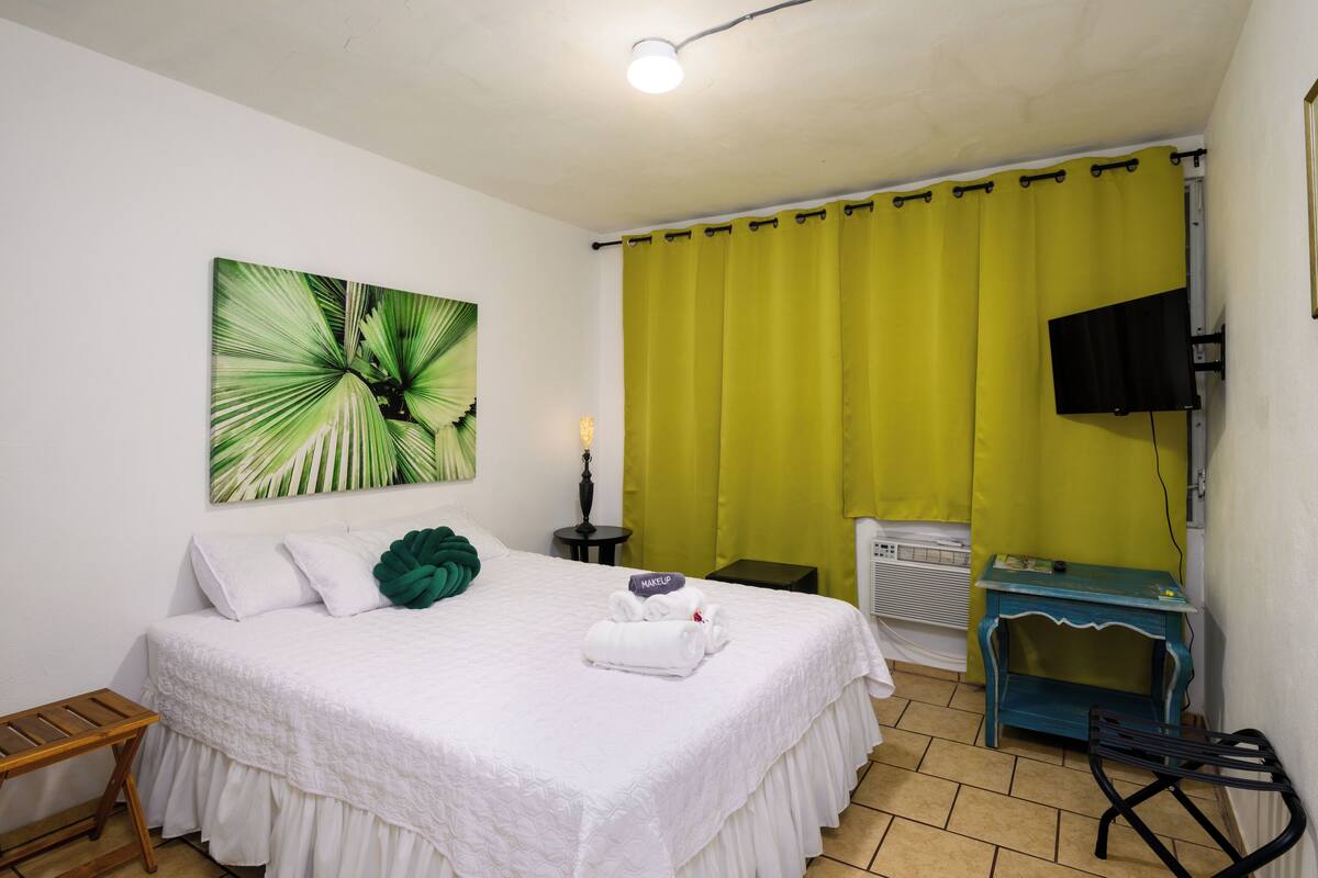 Ein Hotelzimmer mit einem Bett, einem grünen Vorhang, einem Fernseher und einem Bild an der Wand.