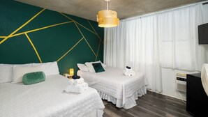 Ein Hotelzimmer mit zwei Betten, einem Wanddesign mit geometrischen Mustern in Grün, einer Deckenleuchte und einem Fernseher auf der rechten Seite.
