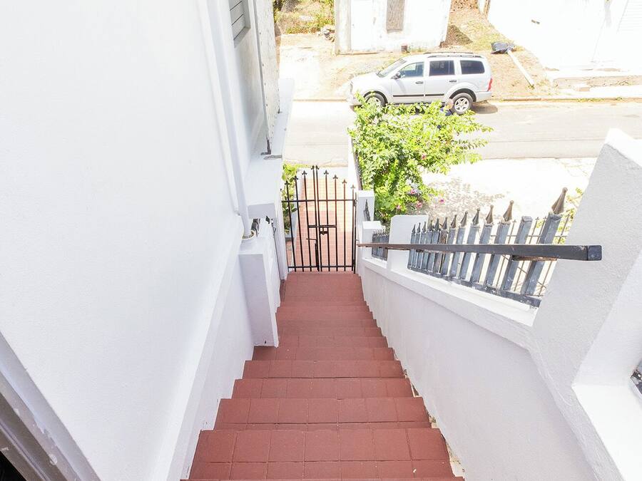 Una escalera conduce a una entrada de paredes blancas, suelo de baldosas rojas y una reja metálica.