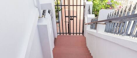 A set of red brick stairs leading to a gated entrance with a white wall on one side and a metal fence on the other.