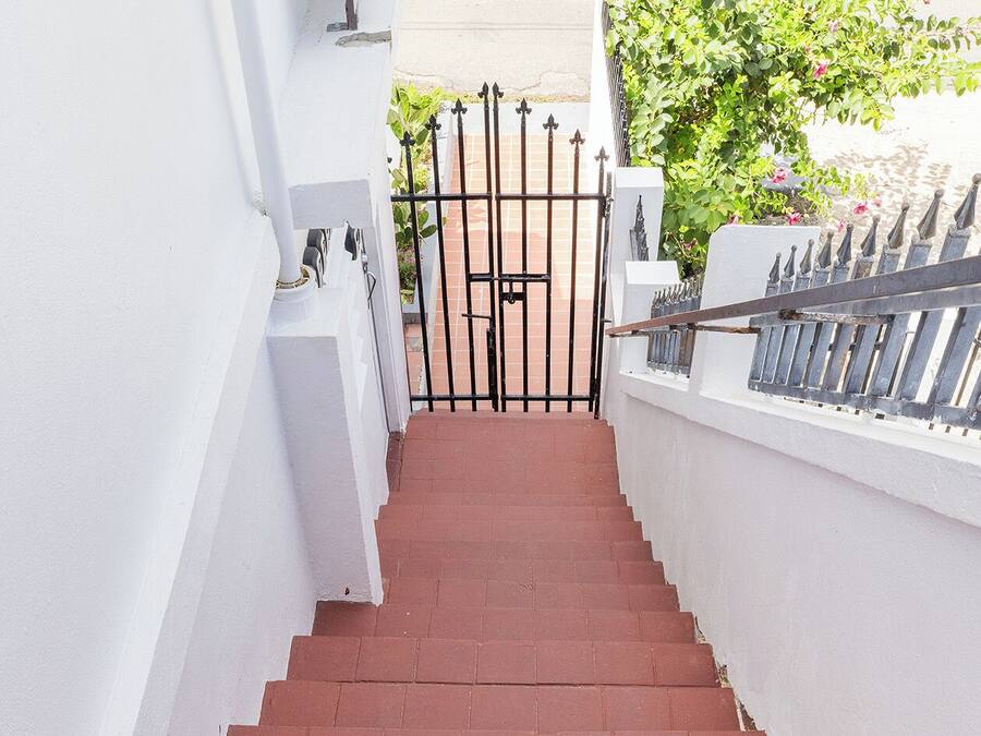 A set of red brick stairs leading to a gated entrance with a white wall on one side and a metal fence on the other.