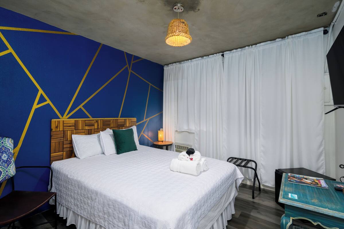 Ein Hotelzimmer mit einem großen Bett, einem hölzernen Kopfteil, einem Nachttisch mit Lampe, einem Schreibtisch und einem Sessel.