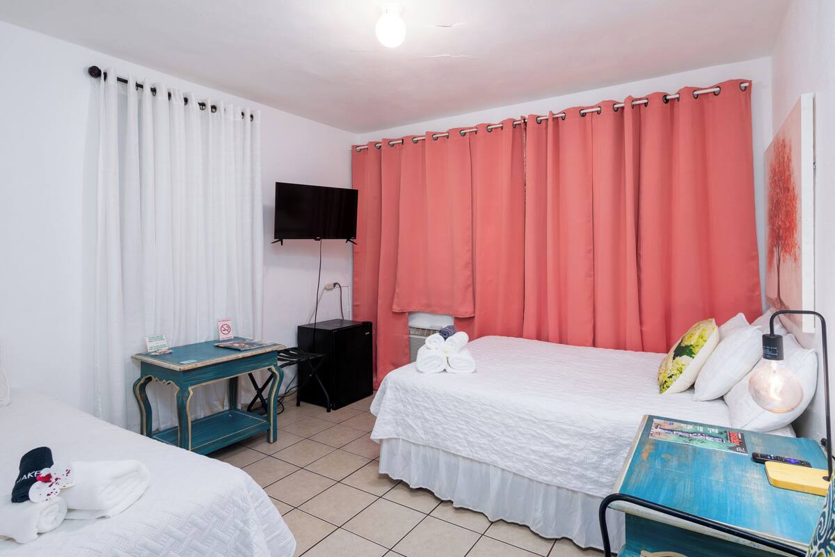 Ein Hotelzimmer mit zwei Betten, einem Schreibtisch, einem Fernseher und einer Lampe.