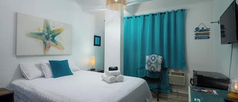 A hotel room with a bed, a desk, a chair, a TV, and a window with curtains.