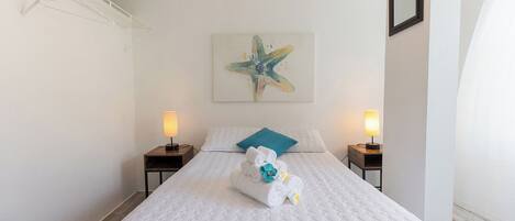 A hotel room with a large bed, two bedside tables with lamps, a star-shaped painting on the wall, and a towel rack.