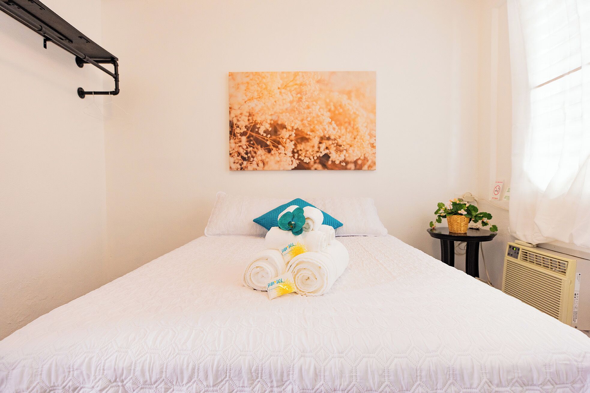 A neatly made bed with rolled towels and a small table with a plant.