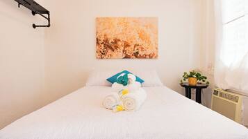 A neatly made bed with rolled towels and a small table with a plant.