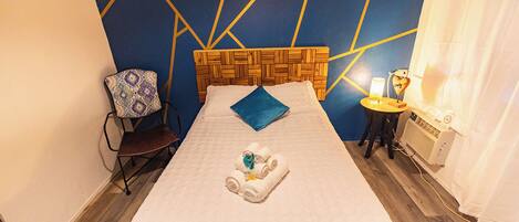 Une chambre d’hôtel avec un lit, une chaise, une petite table avec une lampe et un radiateur.