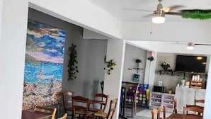 Ein geräumiger Essbereich mit Holztischen und -stühlen, einem Deckenventilator und einem Gemälde mit Strandmotiv an der Wand.