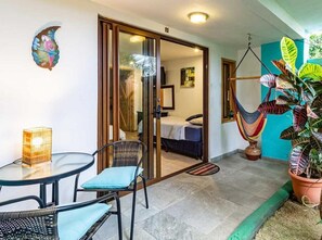 A room with a bed, a glass door leading to a balcony, a hanging chair, and a potted plant. - Posada Nena (Santa Ana)