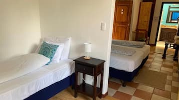 A room with two beds, a small table with a lamp, and a wooden door leading to a bathroom.