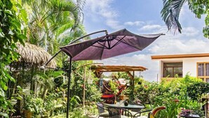 A patio with a table and chairs, surrounded by lush greenery and a thatched roof structure. - Posada Nena (Santa Ana)