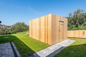 A wooden structure with a door and a small window, surrounded by a well-maintained lawn and a paved path.
