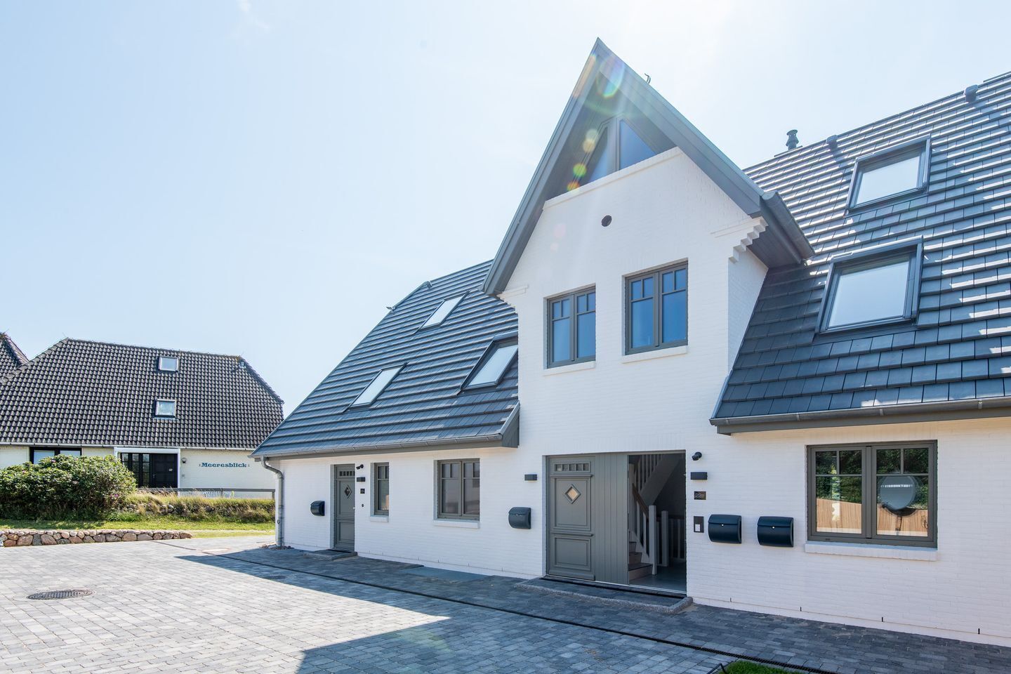 Ein modernes, zweistöckiges Haus mit Satteldach, Eingangstür und einer kleinen Veranda.