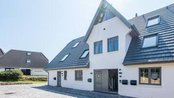 Ein modernes, zweistöckiges Haus mit Satteldach, Eingangstür und einer kleinen Veranda.