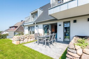 A modern house with a patio, stone walls, and a dining area with chairs and a table. - Haus Dünenweg Whg. 2 - Stilvoll. Modern. Weitblick. - Objekt-id: Odh/22 (Hörnum (Sylt))