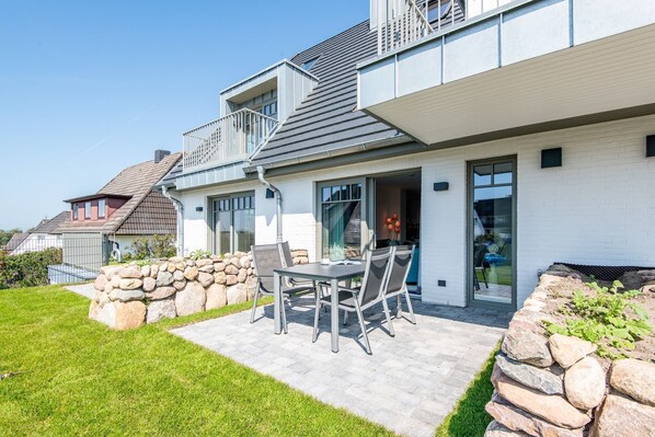 A modern house with a patio, stone walls, and a dining area with chairs and a table.