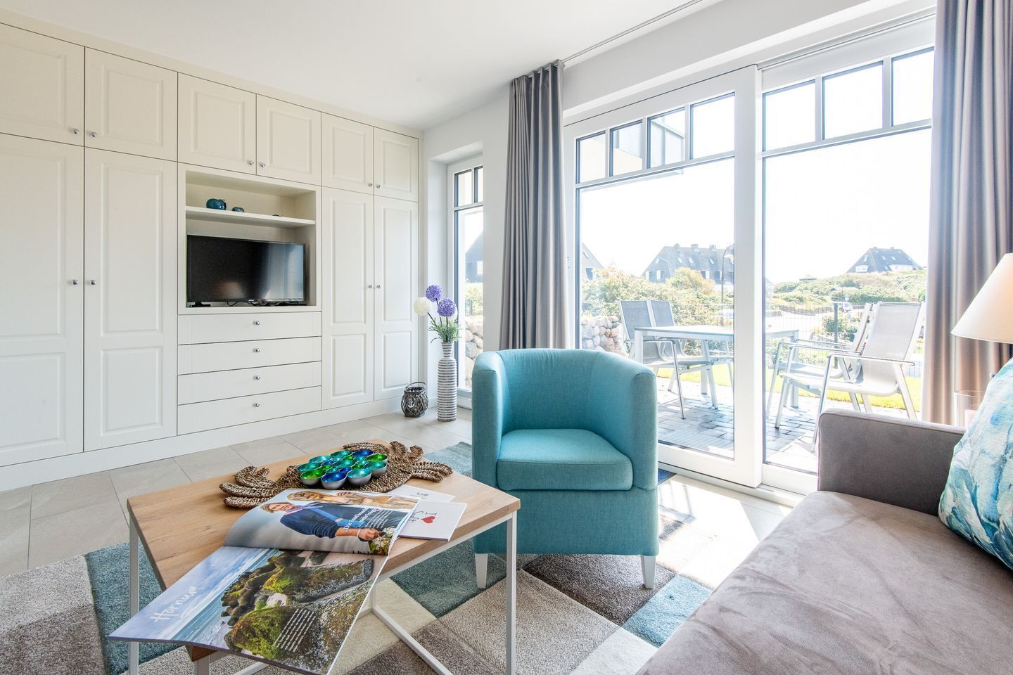 A modern living room with a TV, a blue armchair, a sofa, and a table with magazines.