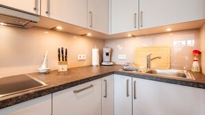 A modern kitchen with white cabinets, a granite countertop, a built-in stove, a coffee machine, and a wooden cutting board.
