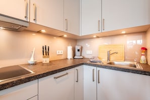 A modern kitchen with white cabinets, a granite countertop, a built-in stove, a coffee machine, and a wooden cutting board.