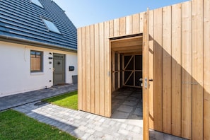 A wooden structure with a door, a white building with a blue roof, and a paved walkway.