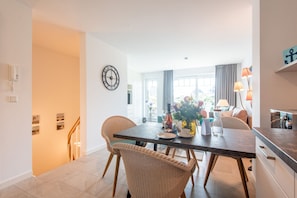 A modern dining area with wicker chairs, a dark wooden table, and a vase of flowers.