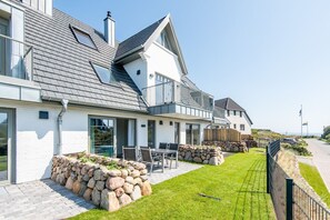 A modern two-story house with a stone foundation, a balcony, and a well-maintained lawn.
